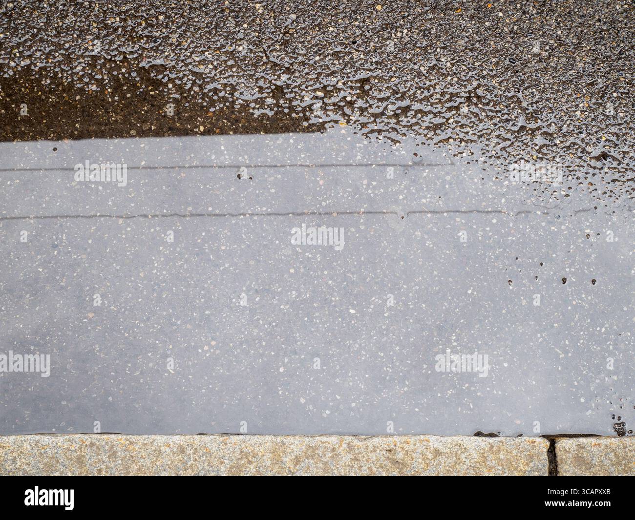 Abstrakter nasser Bürgersteig mit reflektierendem Wasser und rauer Betonstruktur, der eine strukturierte Oberfläche mit schimmernden Lichteffekten schafft Stockfoto