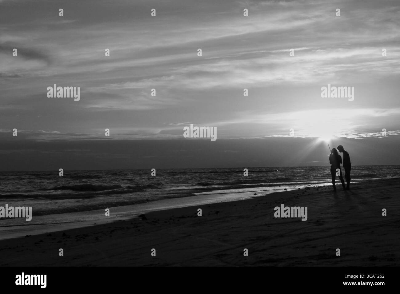 Silhouette eines Paares, das zusammen am Strand bei Sonnenuntergang steht, in Schwarz-weiß Stockfoto