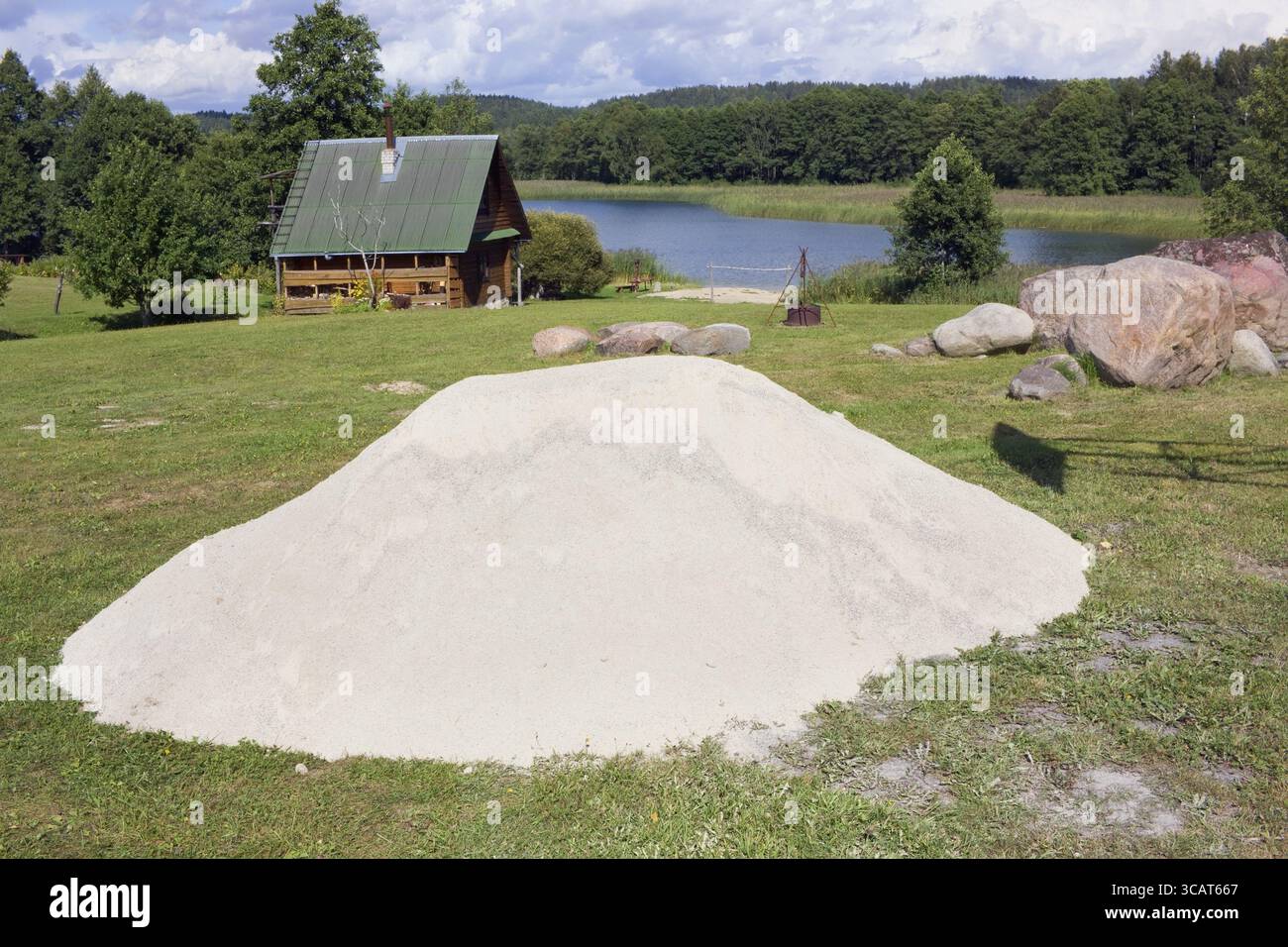 Ein großer Haufen weißen sauberen Flusssandes liegt auf einem Rasen in der Nähe eines Walddorfes. Sonniger Sommer august Tag Natur Landschaft Stockfoto
