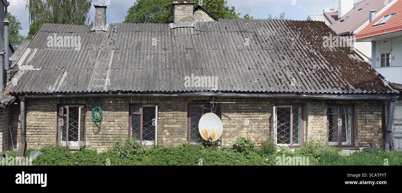 Ruiniert unbewohnten lange Ziegel Baracke in der Mitte von einem modernen Dorf. Sonniger Frühlingstag Panorama-Aufnahme ein. Stockfoto