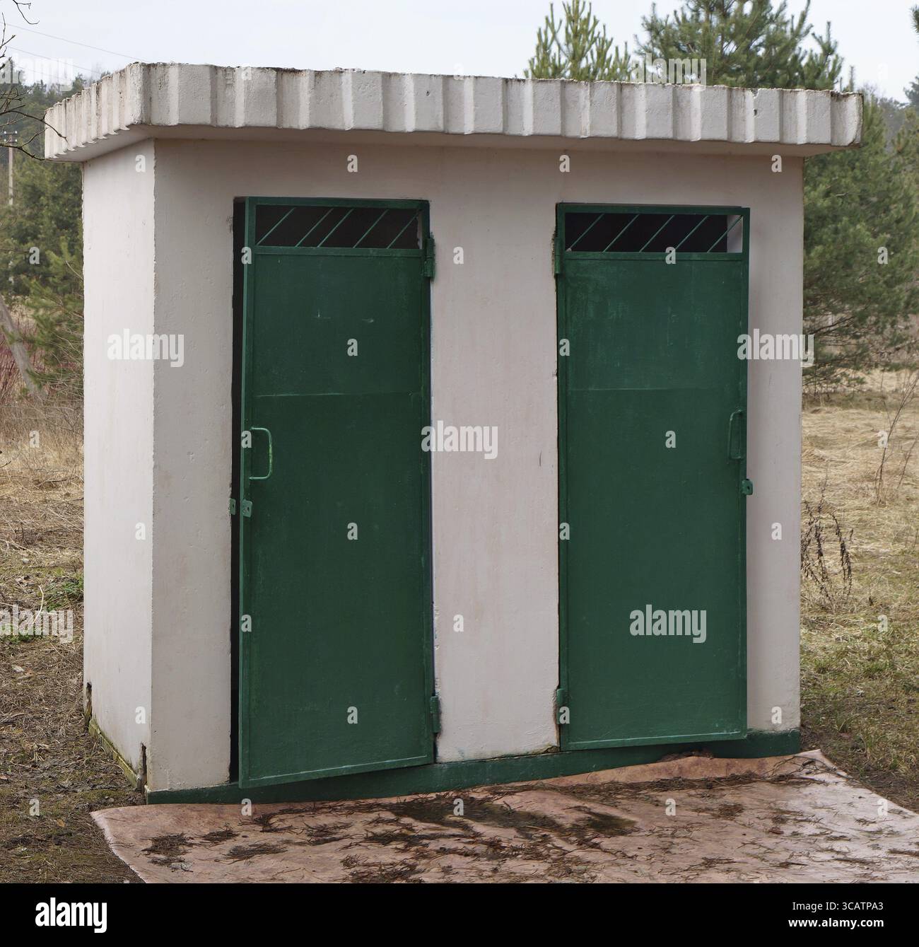 Weiße Backsteintoilette, ländliche handgefertigte öffentliche Parktoilette mit grünen Metalltüren. Sprind Day Outdoor Shot Stockfoto