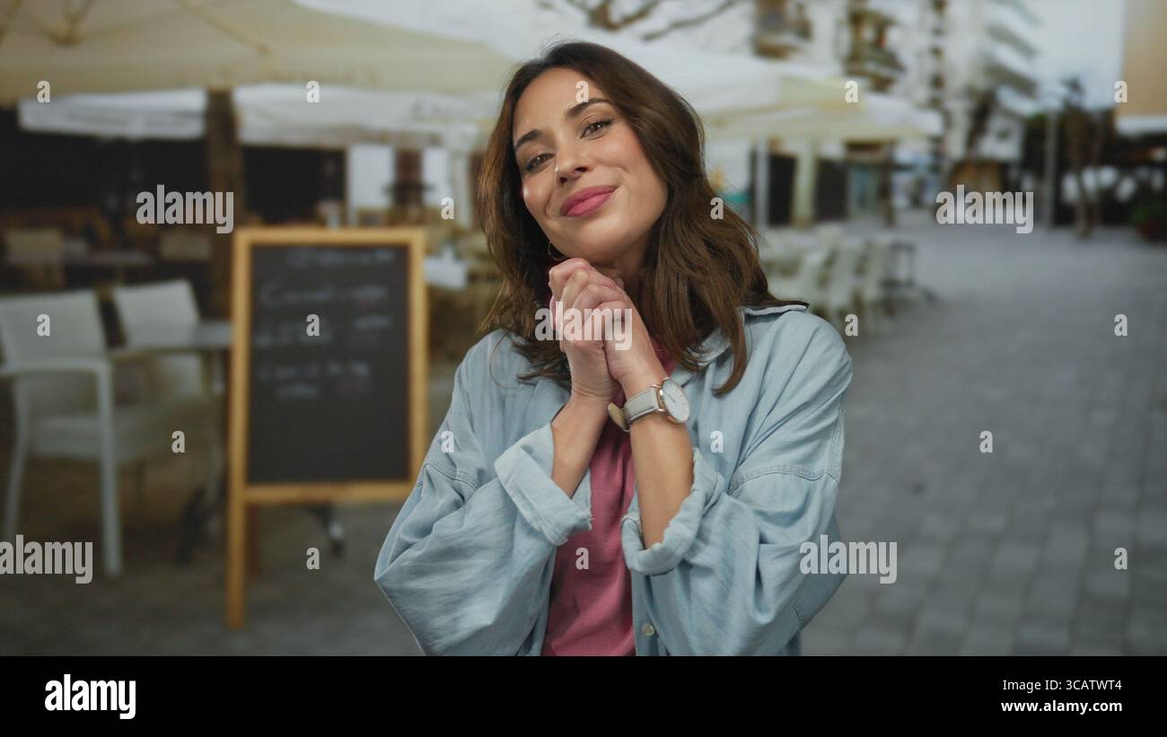 Frau lächelt, während sie auf einer lebhaften Stadterrasse mit Cafés und Restaurants in der Nähe steht und eine fröhliche Atmosphäre ausstrahlt. Stockfoto