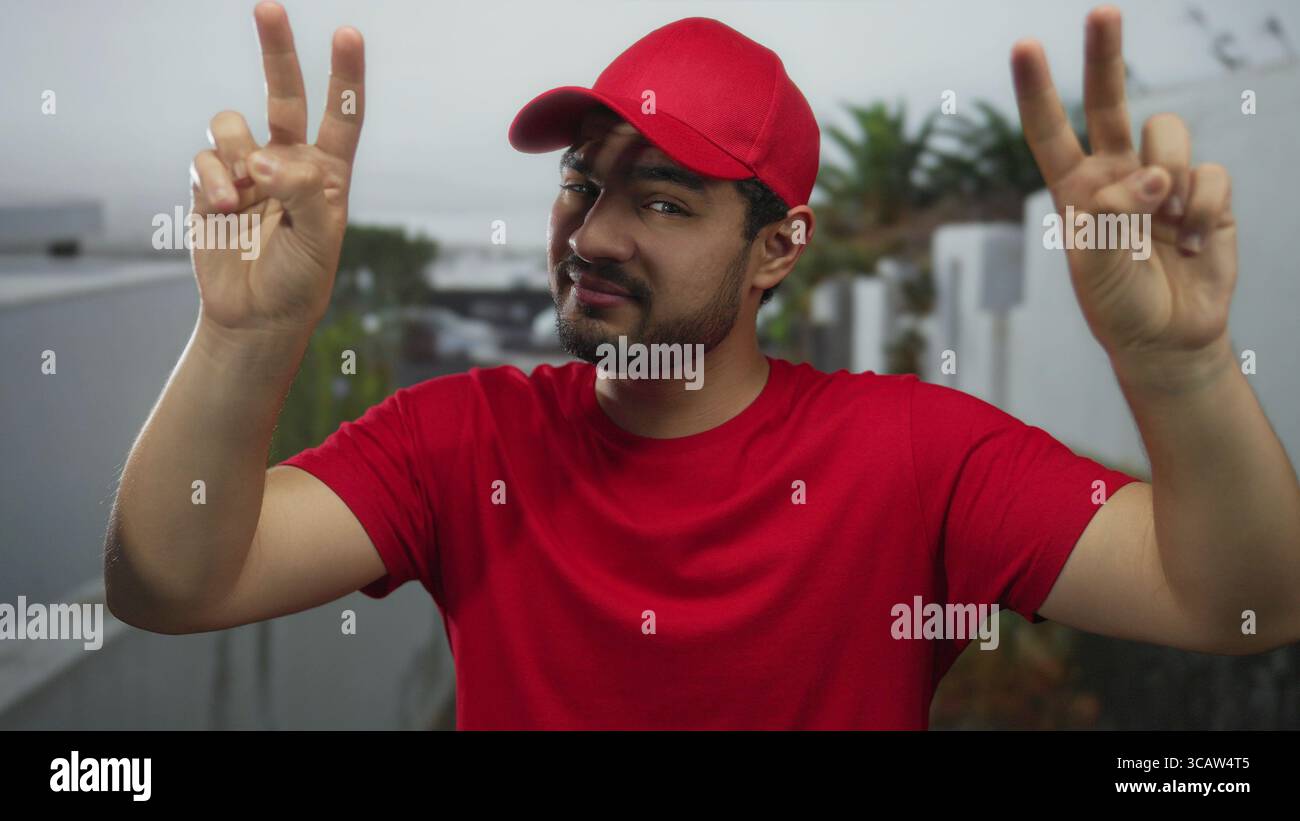 Mann mit rotem Hemd und roter Mütze zitiert auf einer Straße neben einer weißen Gebäudefassade mit Palmenpflanzen im Hintergrund; Sarkasmus. Stockfoto
