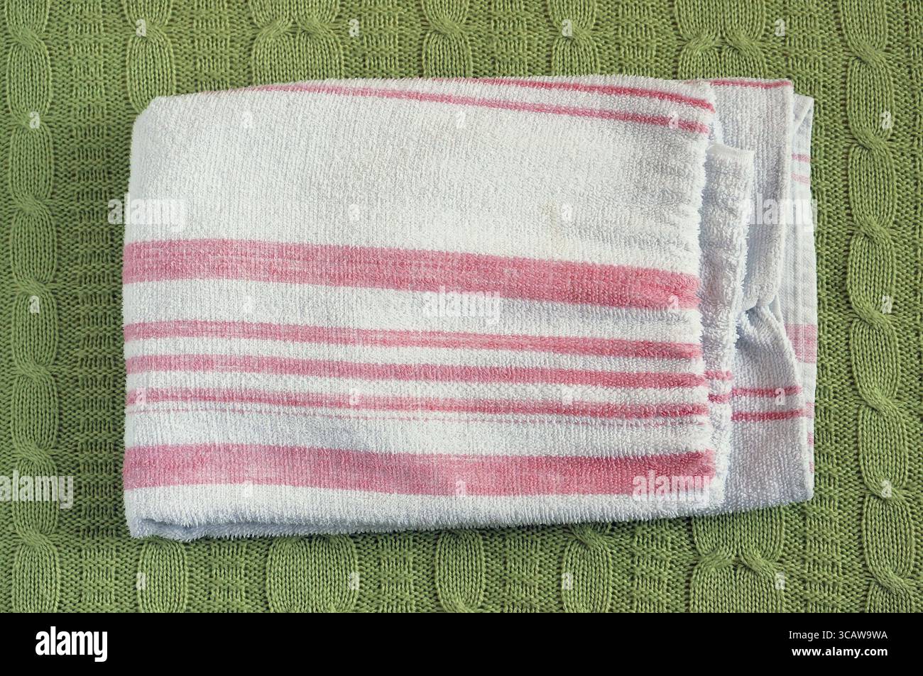Ein weiß gestreiftes, trocken-sauberes Badetuch liegt auf einem Wollgestrick-grünen Bettbezug Stockfoto