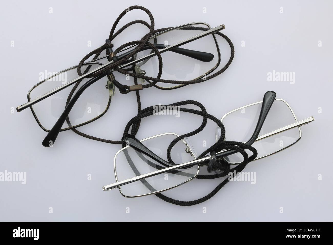 Die alte Brille meines Großvaters steht auf einem weißen Tisch. Einfacher Stahlrahmen aus Kunststoffgläsern und Nackenriemen Stockfoto