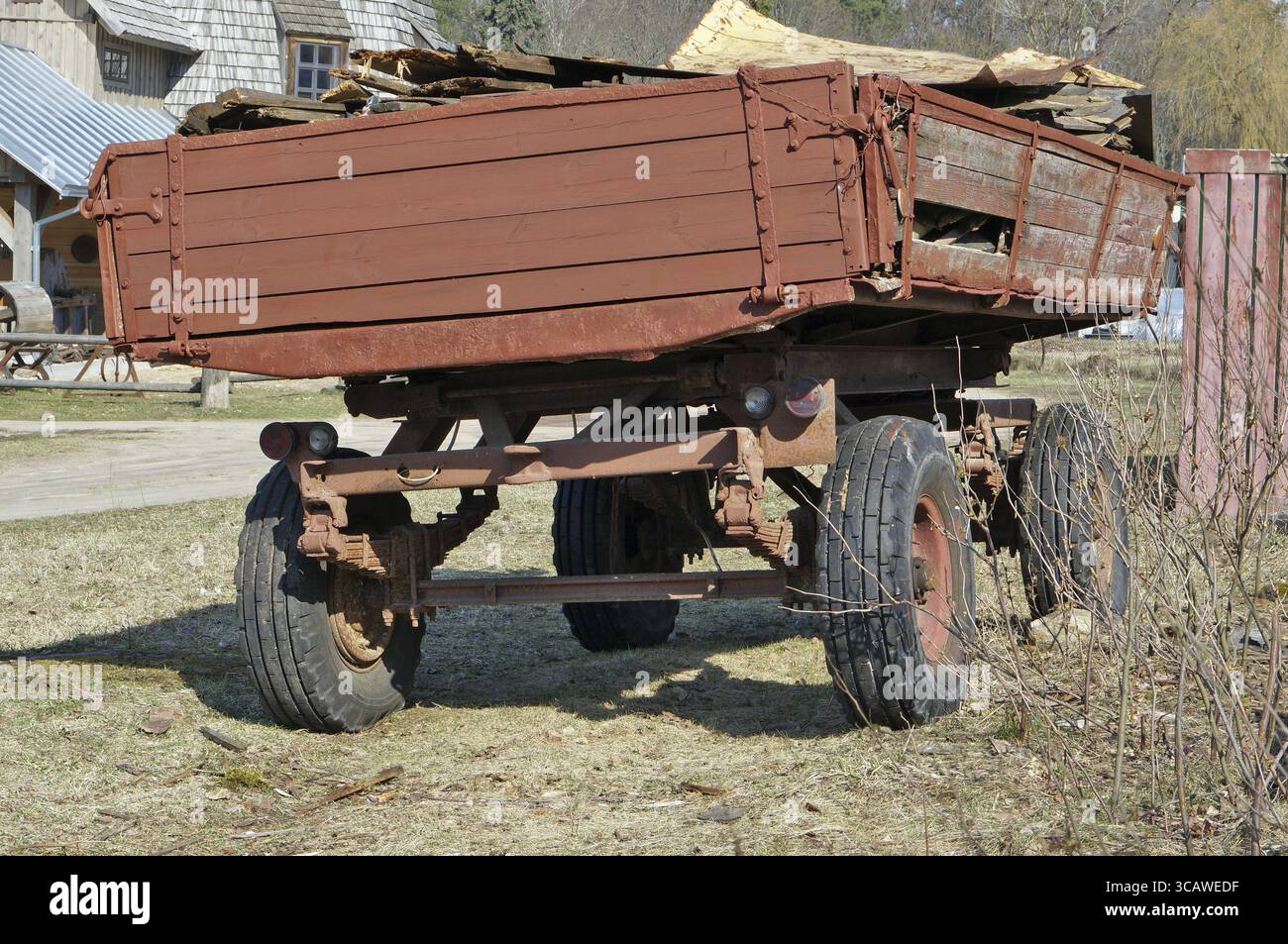 Alter roter defekter Traktor-Anhänger-Wagen auf dem Dorf. Sonniger Frühlingstag im Freien Stockfoto