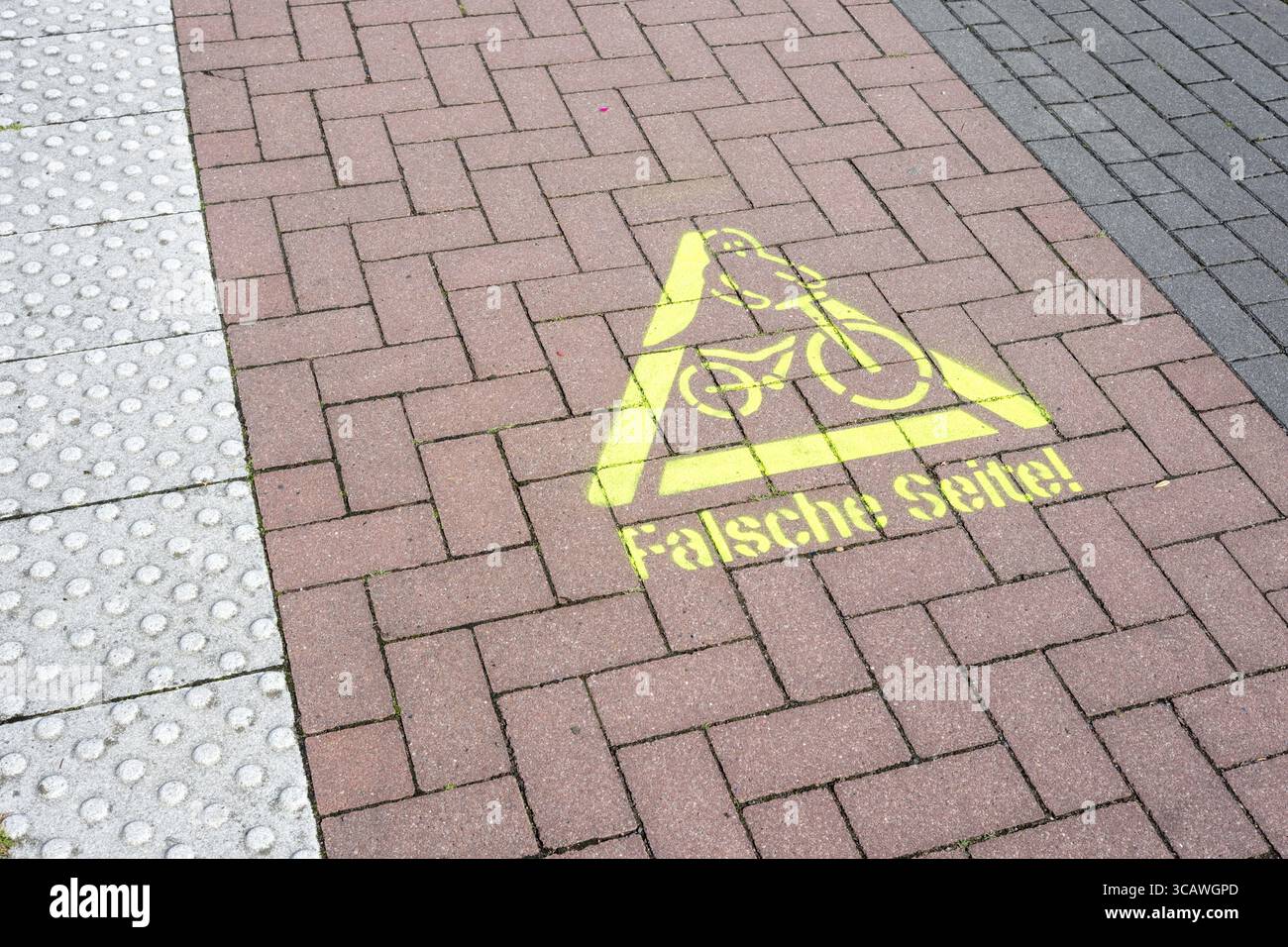 Gelbes Warnschild auf einer deutschen Kopfsteinpflasterstraße, das darauf hinweist, dass Radfahrer in die falsche Richtung gehen Stockfoto