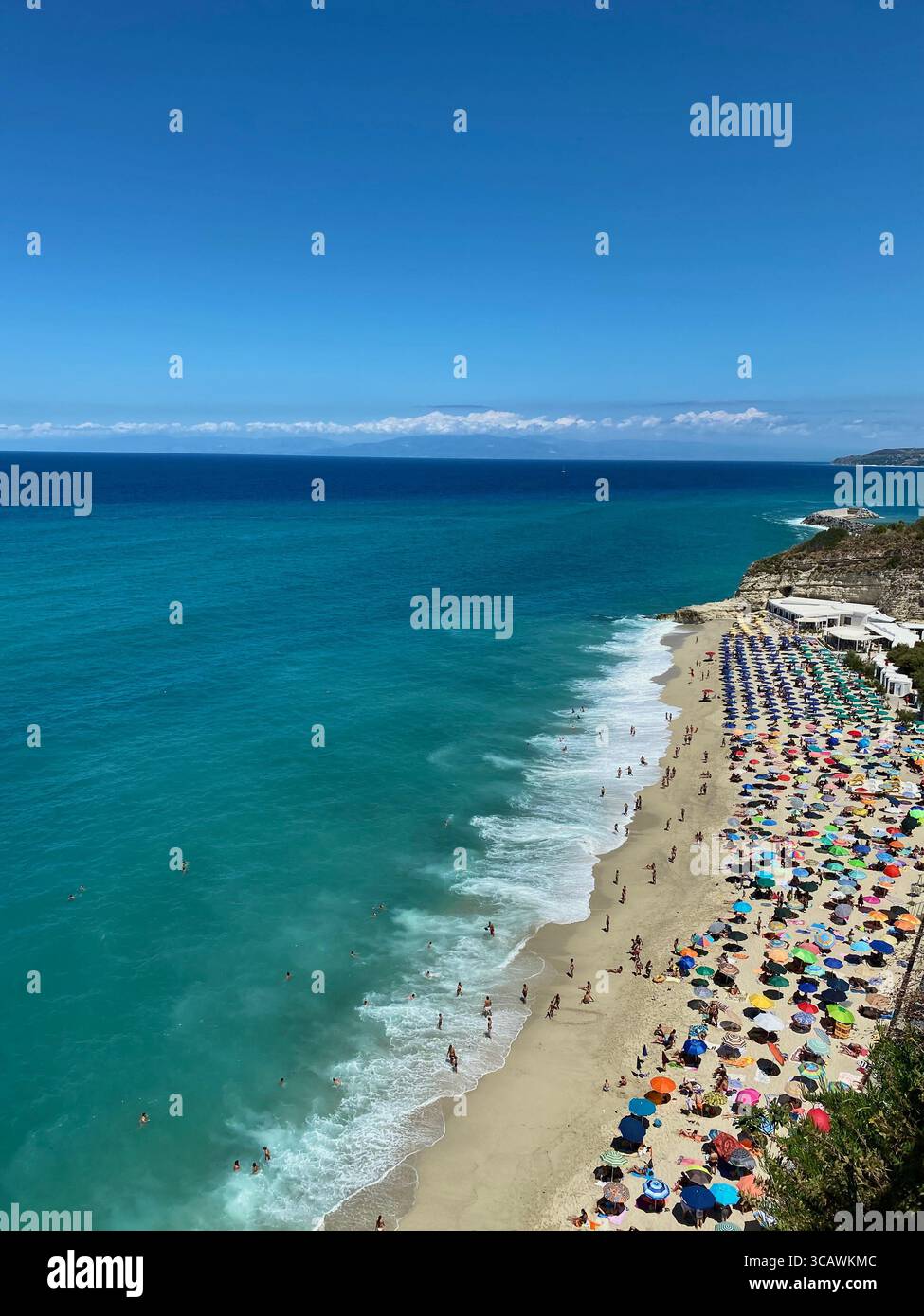Blick von oben auf einen überfüllten Strand mit bunten Sonnenschirmen und türkisfarbenem Wasser in Tropea, Kalabrien, Italien - Smartphone-aufgenommenes Stockfoto