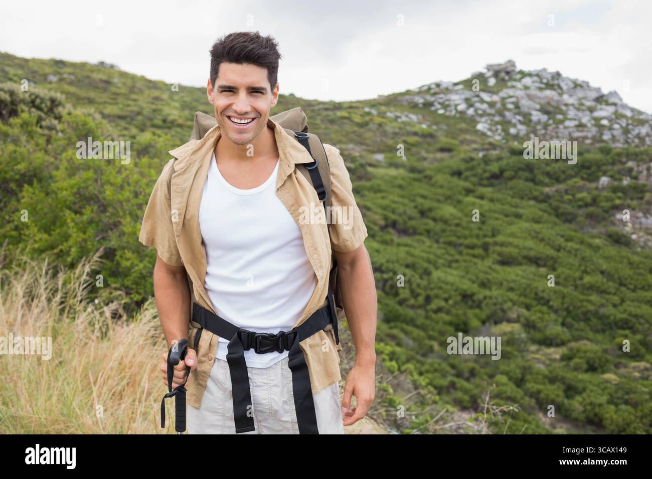 Ein Mann in seinen Zwanzigern, der auf einem schmalen Bergweg steht, einen Wanderstock hält und einen Rucksack trägt Stockfoto