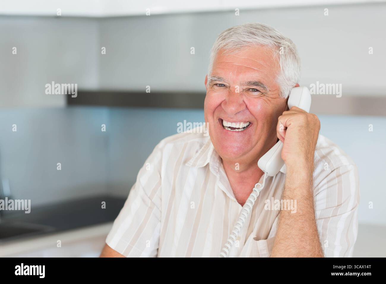 Senior Mann, der über schnurgebundenes Telefon in moderner Küche mit Arbeitsplatte und Schränken, Kopierraum spricht Stockfoto
