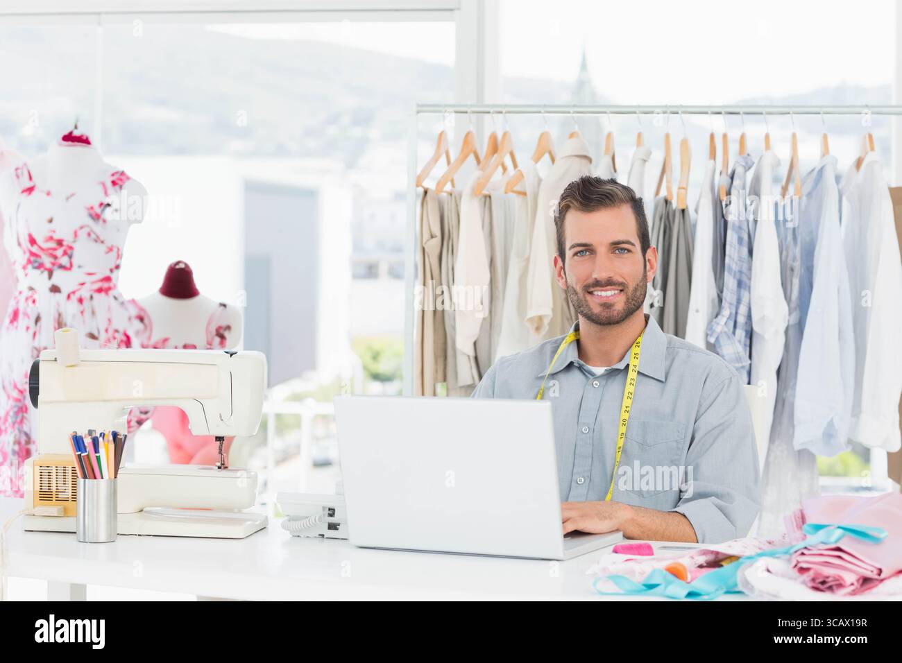 Männlicher Designer, der im Designstudio arbeitet und Entwürfe mit Laptop, Nähmaschine und Kopierraum skizziert Stockfoto