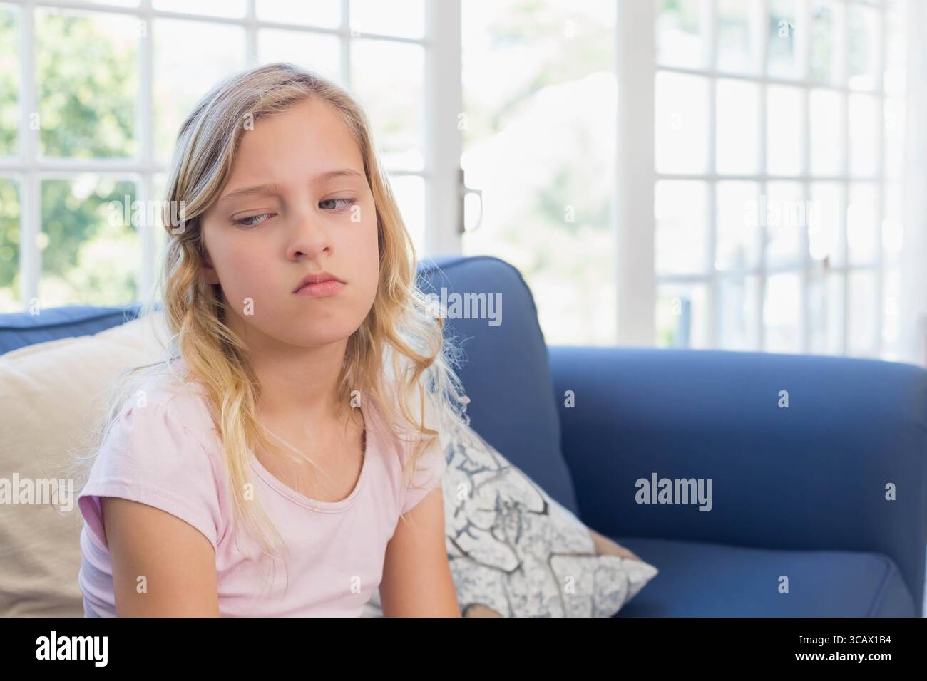 Mädchen, das zu Hause auf blauem Sofa sitzt und sich auf einem Kissen stützt und auf die Glasfenster und den Kopierraum blickt Stockfoto