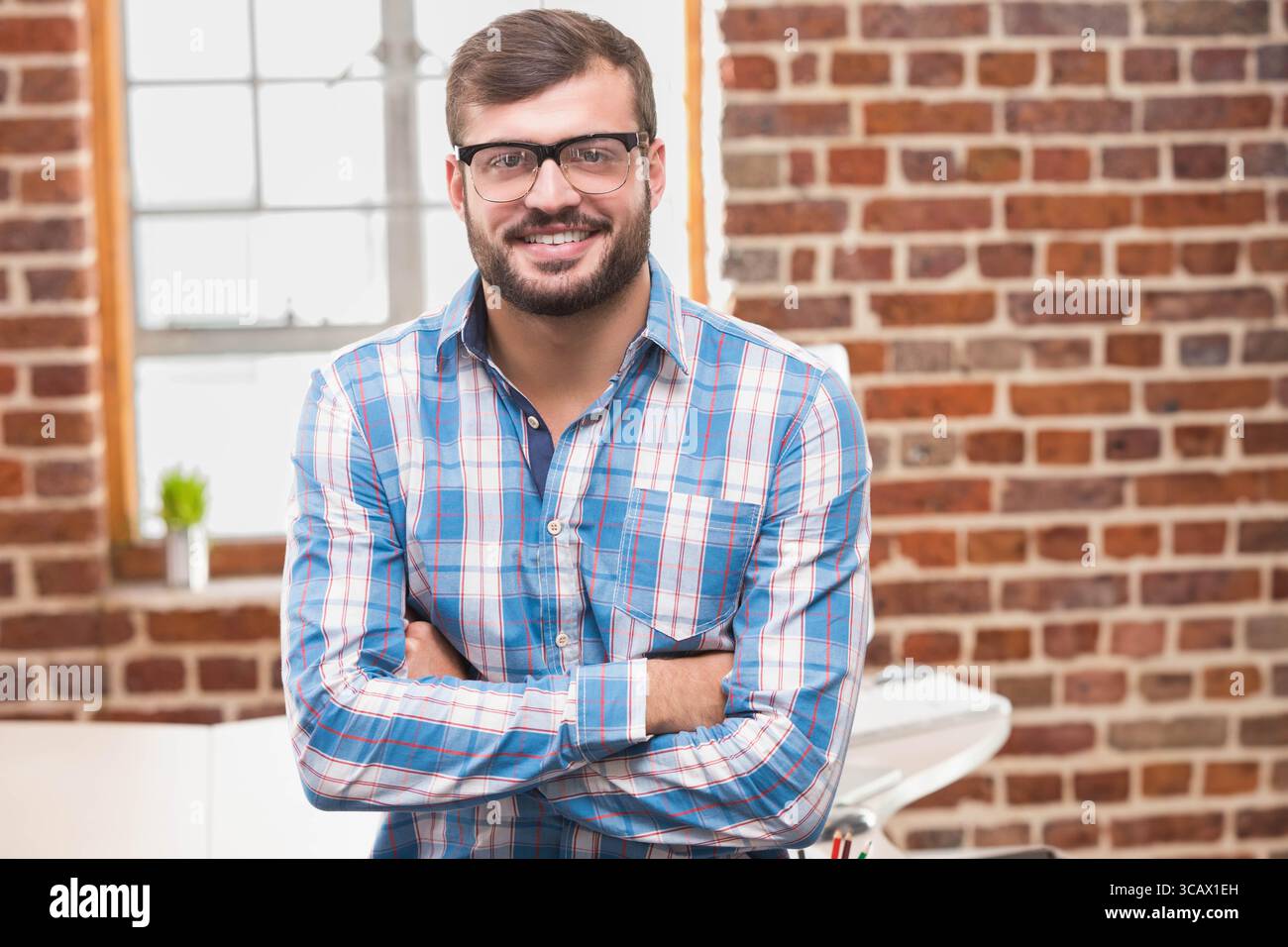Afroamerikaner, der im Loft-Büro am weißen Schreibtisch steht und farbige Stifte und saftige Stifte hält Stockfoto