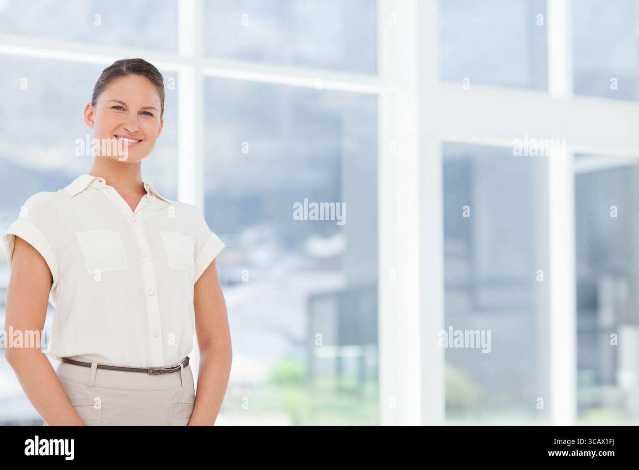 Weibliche Geschäftsfrau, die neben Glasfenstern im Büro steht und einen schmalen Gürtel und Kopierraum zeigt Stockfoto