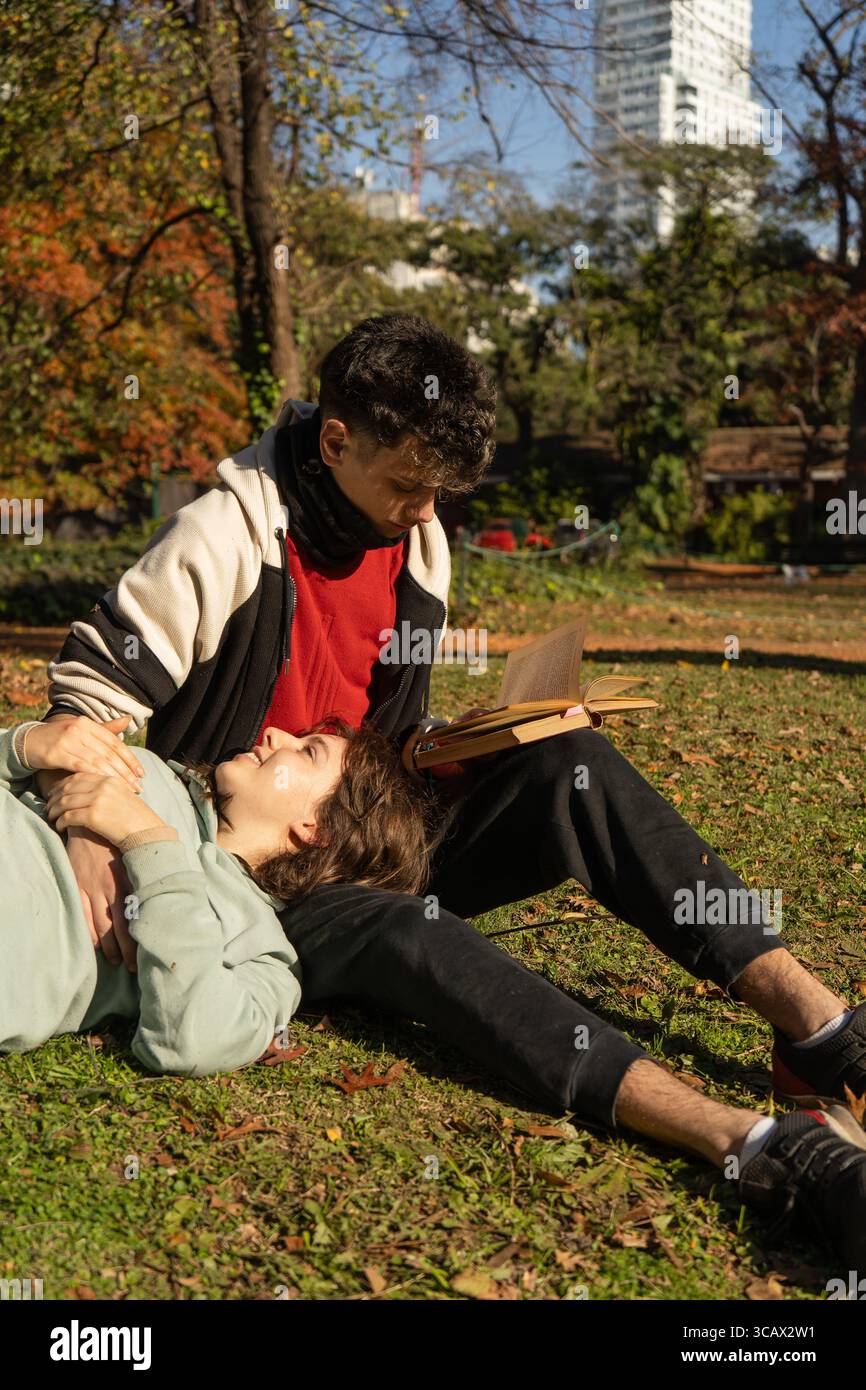 Junge Paare, die einen entspannten Nachmittag verbringen und gemeinsam ein Buch im Park lesen Stockfoto