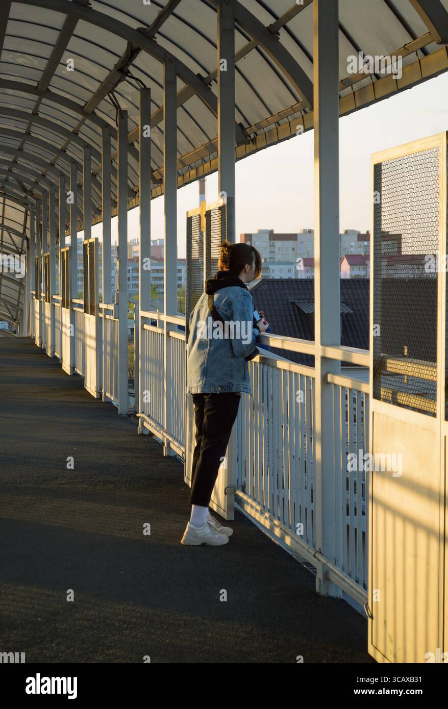 Ein Mädchen in einer Jeansjacke lehnt sich auf das Geländer einer Fußgängerbrücke und blickt in die Ferne Stockfoto