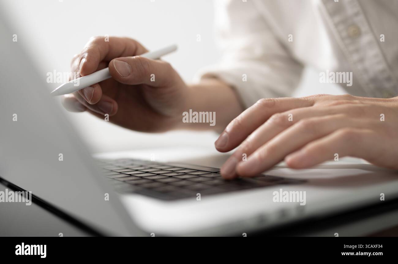 Eine Nahaufnahme der Hände eines Mannes, die mit einem Stift an einem Laptop arbeiten und damit Produktivität, digitalen Workflow und moderne geschäftliche oder kreative Aufgaben symbolisieren Stockfoto