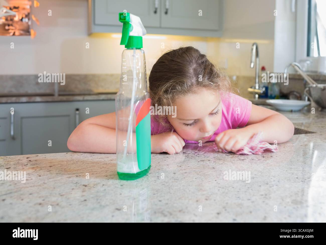 Kinderreinigung Granitarbeitsfläche in der Küche mit Sprühflasche und rosafarbenem Tuch, Kopierraum Stockfoto