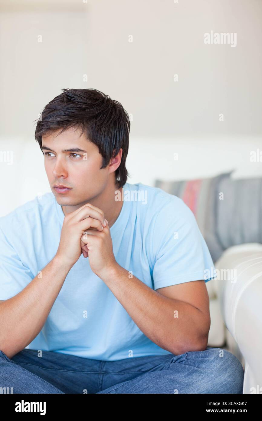 Weißer Mann, der sich auf ein helles Sofa im Wohnzimmer mit Kissen lehnt und den rechten Kopierraum sieht Stockfoto