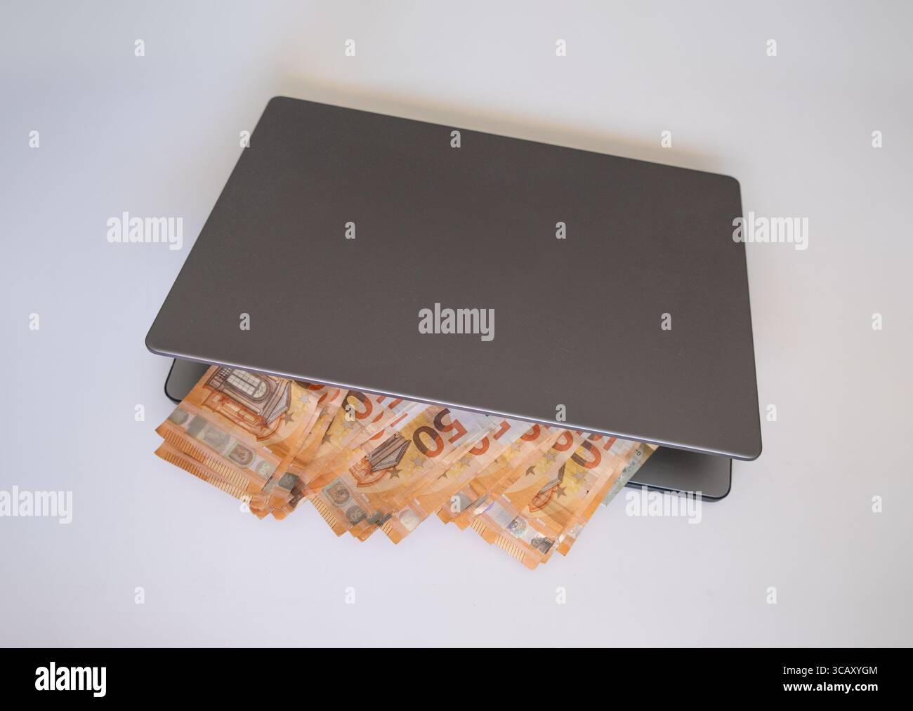 Geänderte 50-Euro-Rechnungen, die aus einem geschlossenen Laptop herausragen. Konzept von verborgenen Einkünften, digitalen Spareinlagen, Cyberkriminalität oder Online-Vermögen. Stilisiertes Finanzbild Stockfoto