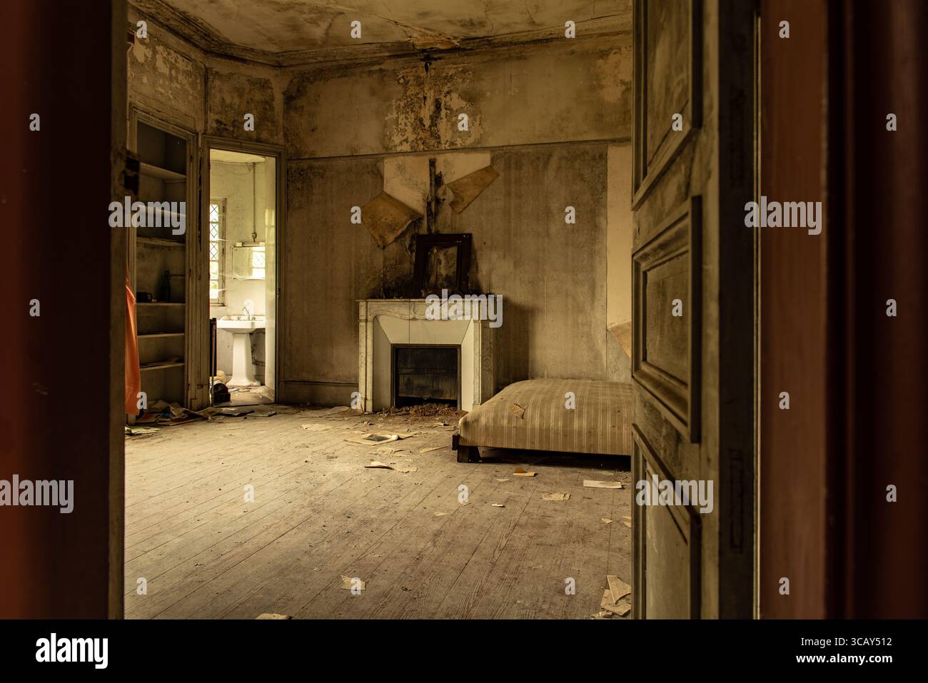 Verlassener Raum mit verrottetem Kamin und Matratze im verfallenen französischen Schloss, Tageslicht, das die urbane Erkundungsszene unterstreicht Stockfoto