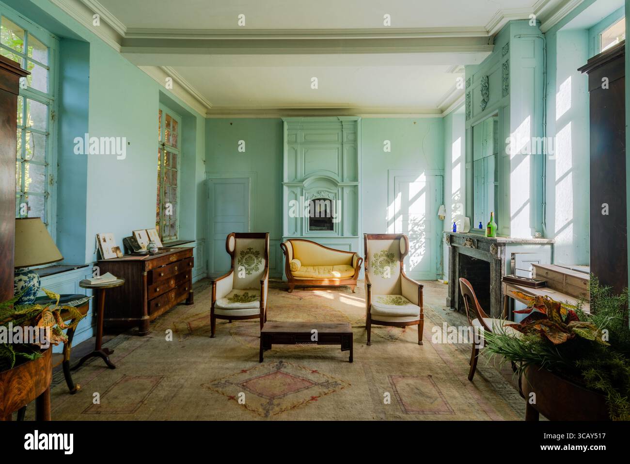 Ein verlassenes, sonnendurchflutetes Wohnzimmer mit Vintage-Möbeln und pastellblauen Wänden in einem vergessenen französischen Schloss Stockfoto