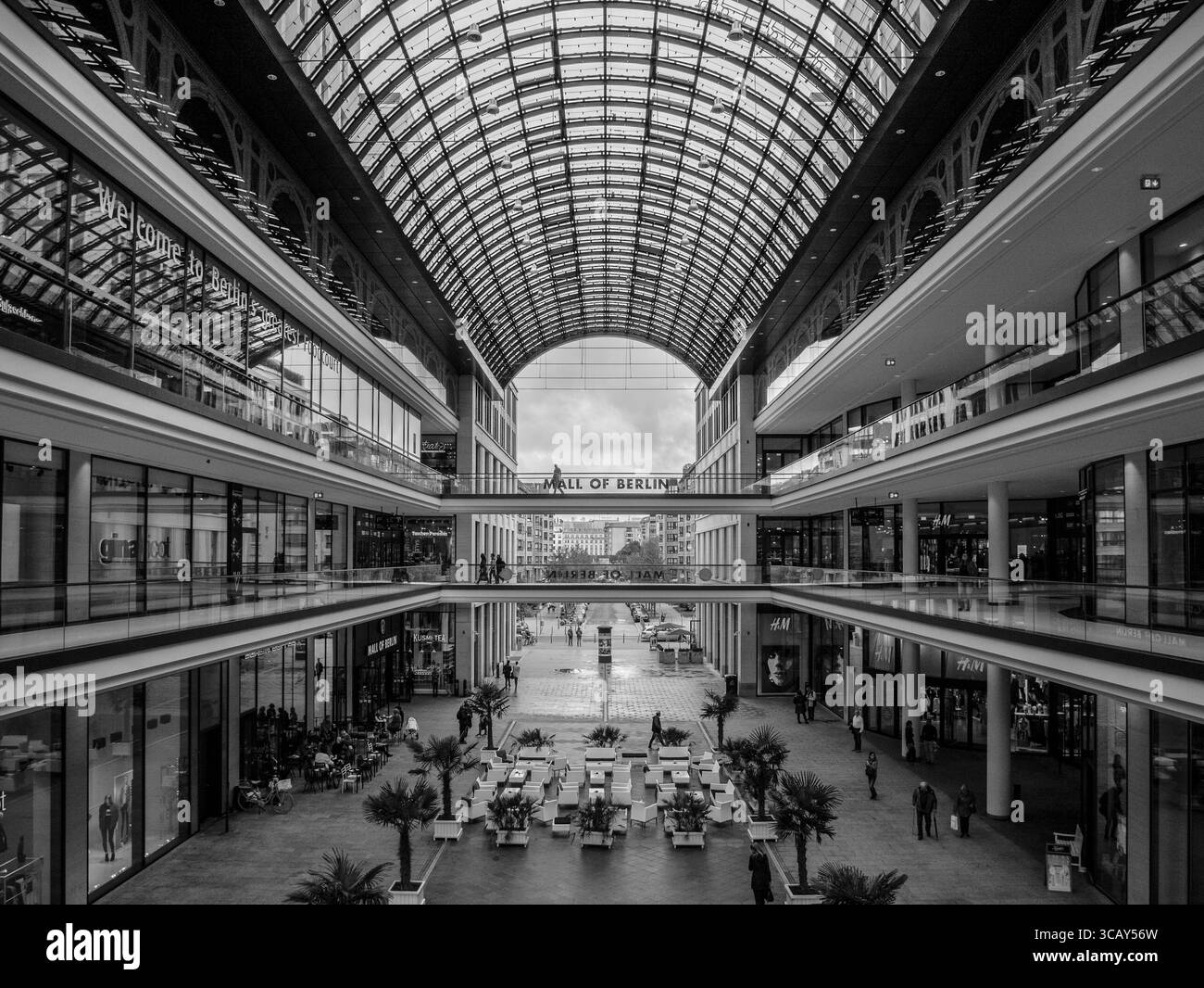 Innenblick auf die moderne Mall von Berlin mit Glasdecke, geräumigen Gehwegen und Einkaufsmöglichkeiten in einer lebhaften urbanen Umgebung Stockfoto
