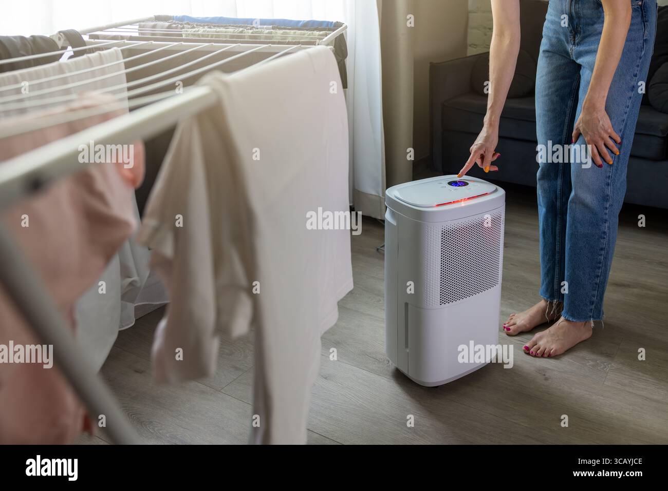Die Frau hat zu Hause im Zimmer einen Luftentfeuchter eingerichtet. Luftfeuchtigkeitsregelung, Feuchtigkeitsreduzierung Stockfoto