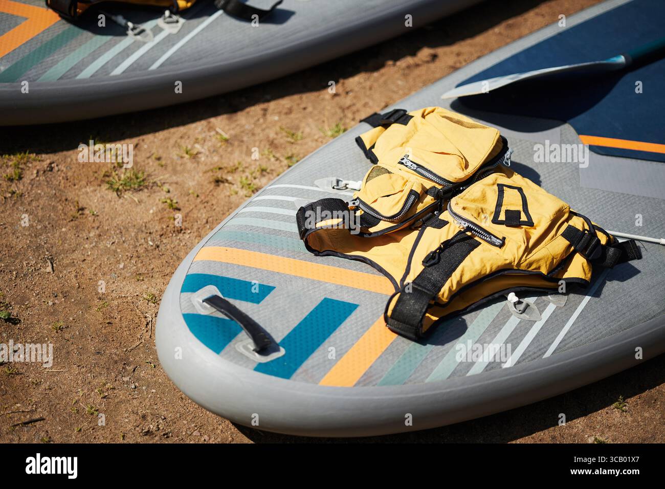 Die Nahaufnahme zeigt ein Paddleboard mit Paddel und Schwimmweste, das draußen auf dem Boden liegt und die wichtige Sicherheitsausrüstung für Wassersport und Freizeitaktivitäten hervorhebt Stockfoto