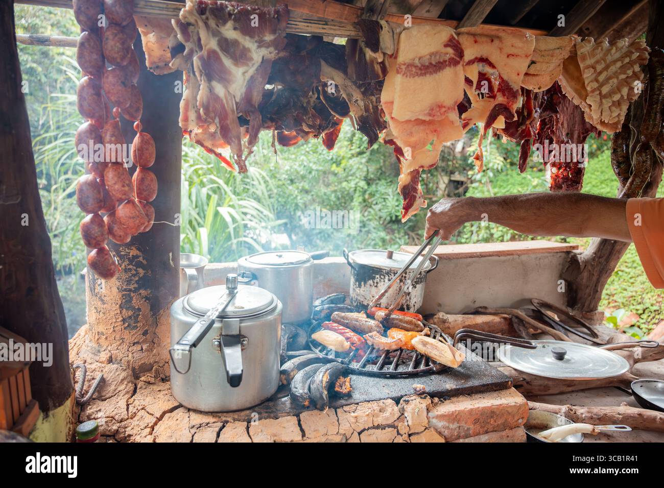 Nahaufnahme von hängenden Chorizos und geräuchertem Fleisch über einem rustikalen Holzofen in einer kolumbianischen Landküche. Authentische Lebensmittelkonservierung und Gril Stockfoto