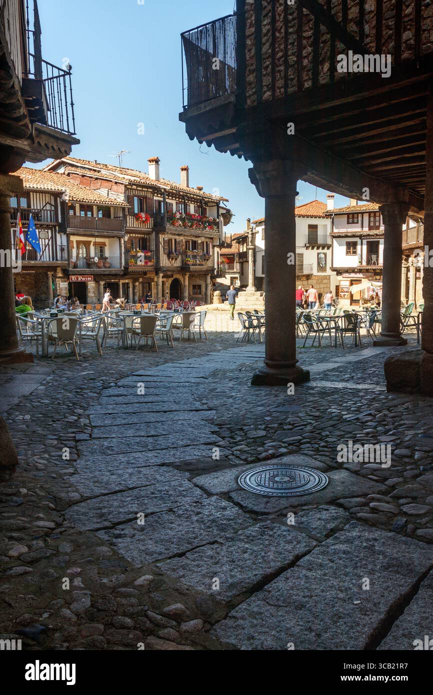 La Alberca, Spanien . 31.5.2024: Kopfsteingepflasterte Straße mit Arkaden im Schatten, mit dem Plaza Mayor im Hintergrund, beleuchtet von der Sonne in der Villa Stockfoto