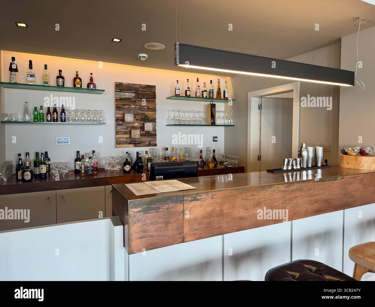 Moderne Hotelbar mit Holztheke, hinterleuchteten Regalen mit Flaschen, Glaswaren und warmer Beleuchtung im Lince Nordeste Country Hotel. Stockfoto