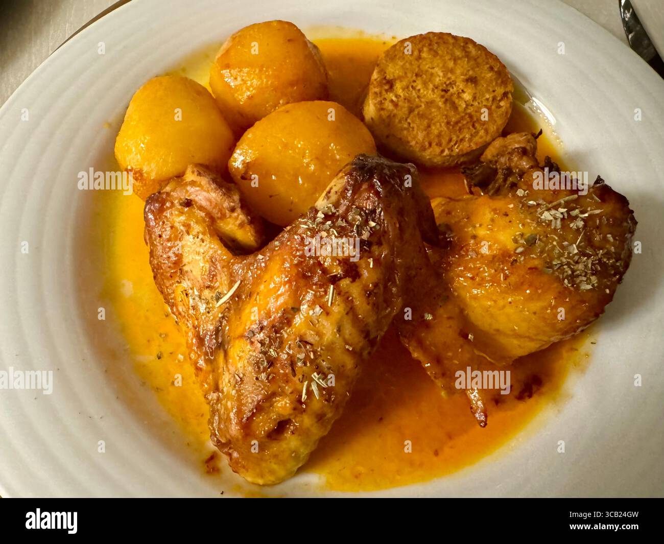 Teller mit gebratenen Hähnchenflügeln mit goldenen Kartoffeln und einer herzhaften Sauce, serviert auf einem weißen Teller. Stockfoto