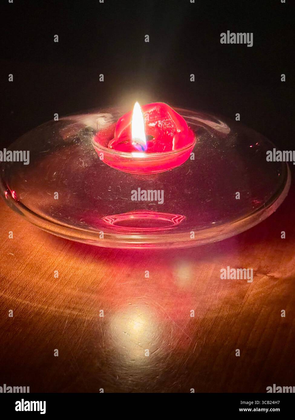 Einzelne rote schwebende Kerze, die sanft auf klarem Wasser in einer Glasschale brennt, schafft ein warmes, intimes Ambiente. Stockfoto