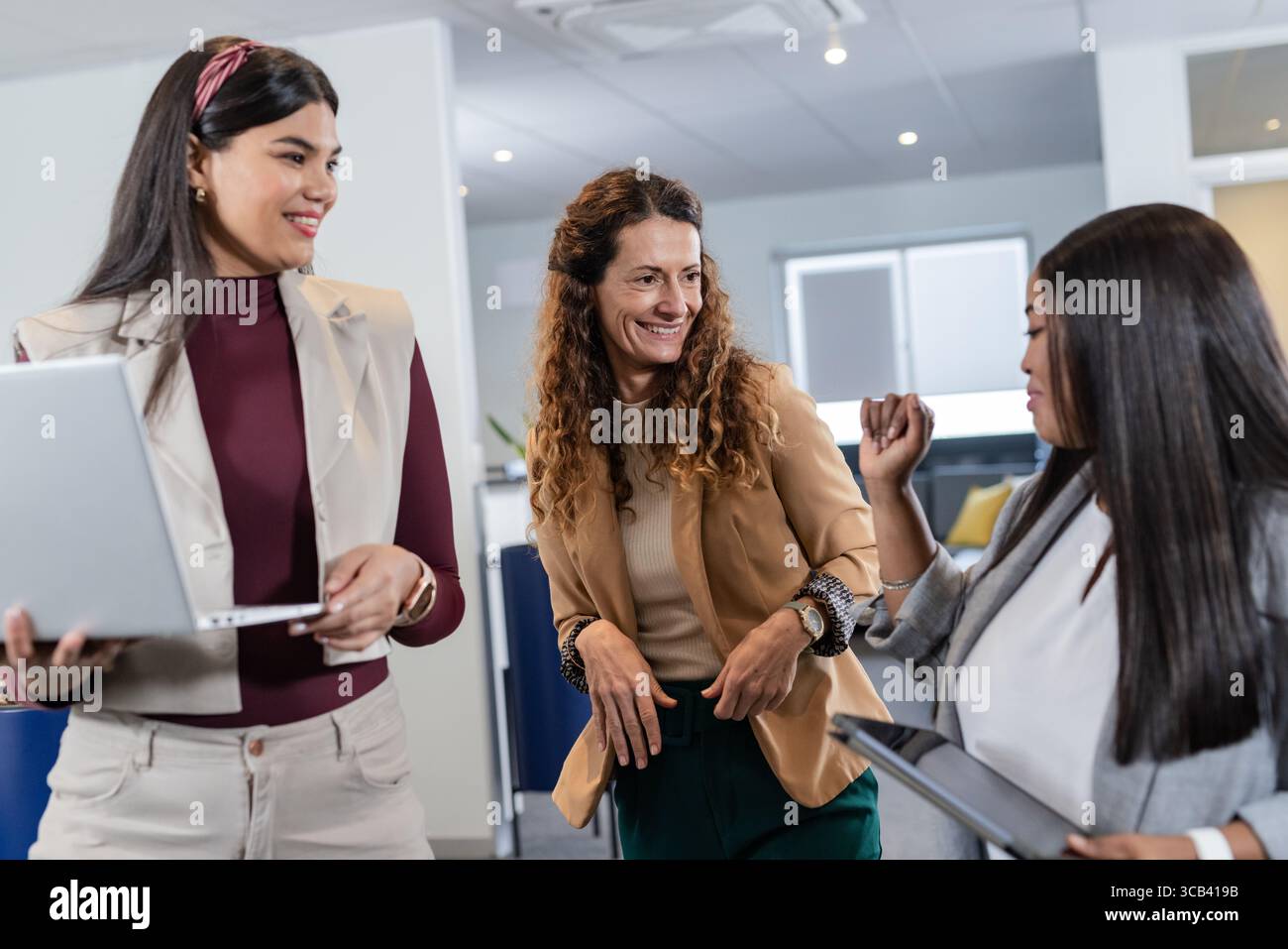 Verschiedene Kolleginnen, die Blazer tragen, arbeiten an Workstations mit Laptop und Tablet zusammen Stockfoto