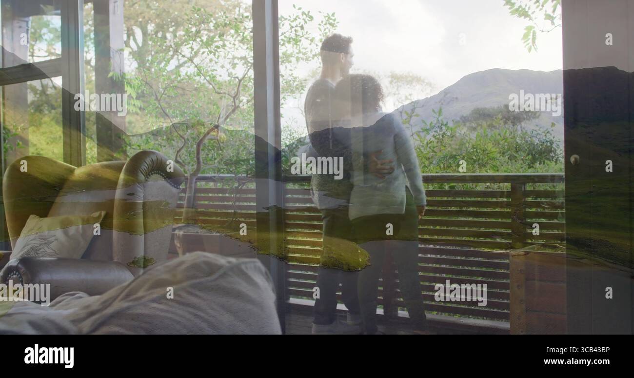 Stehendes Paar mit Blick auf die Glastür des Zimmers auf ein hölzernes Balkongeländer, mit Sofa und Sessel Stockfoto