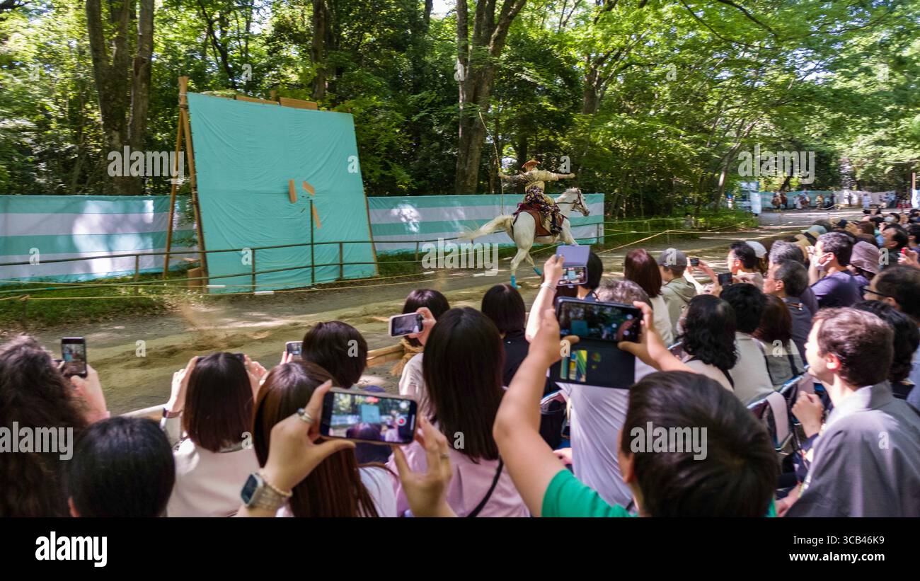 Eine lebhafte Outdoor-Szene zeigt eine traditionelle Bogenschießen-Performance, die ein großes Publikum während des Yabusame Shinji Festivals in Kyoto, Japan, fesselt Stockfoto