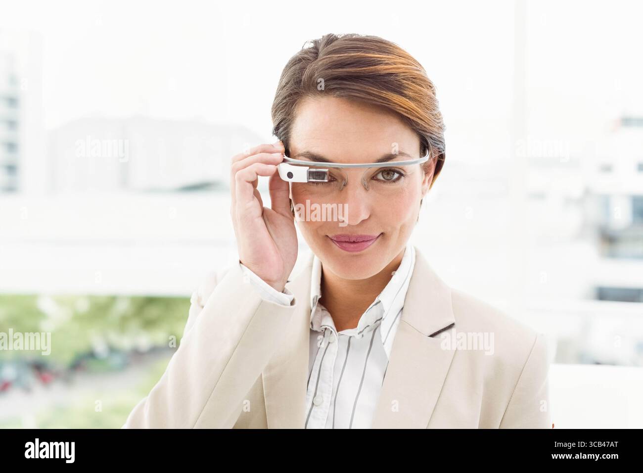 Hellhäutige Geschäftsfrau mit Blazer und verstellbarer Augmented-Reality-Brille am Bürofenster Stockfoto