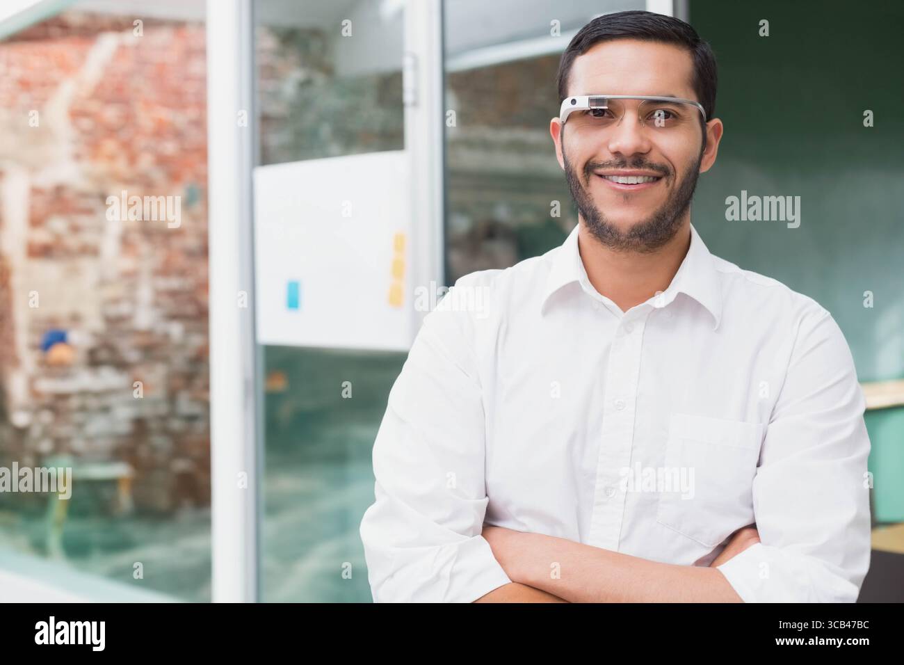 Mann mit weißem Hemd und einer klugen Brille, die Arme im Büro überkreuzt und grüne Tafel zeigt Stockfoto