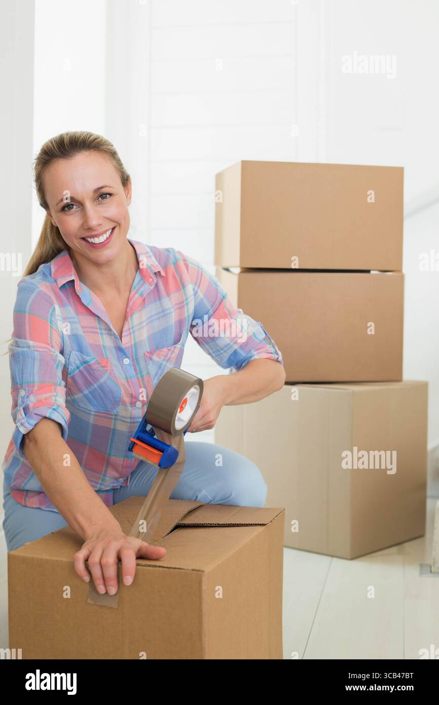 Mittelgroße Erwachsene Frau kniend auf Holzboden im Eingangsbereich mit tragbarem Bandspender Stockfoto
