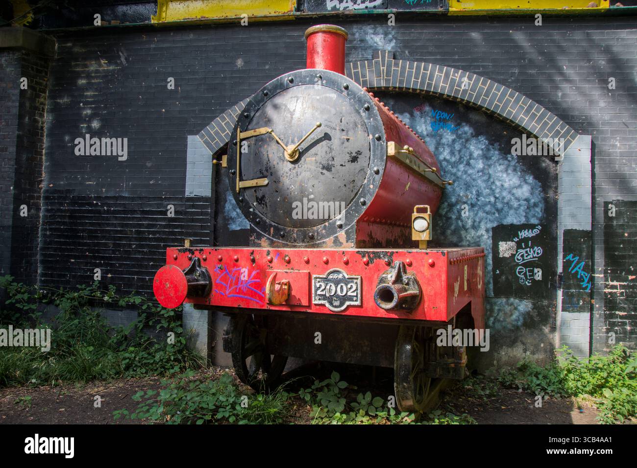 Little Red Train, eine lebensgroße rote Dampflokomotive, die aus einem Tunnel unter einer Brücke hervorgeht Stockfoto
