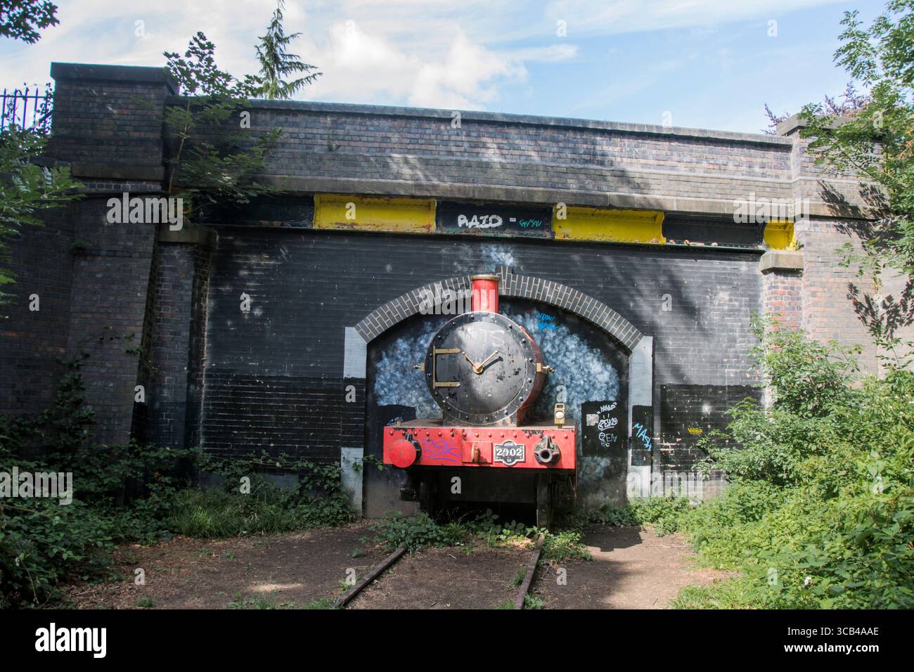 Little Red Train, eine lebensgroße rote Dampflokomotive, die aus einem Tunnel unter einer Brücke hervorgeht Stockfoto