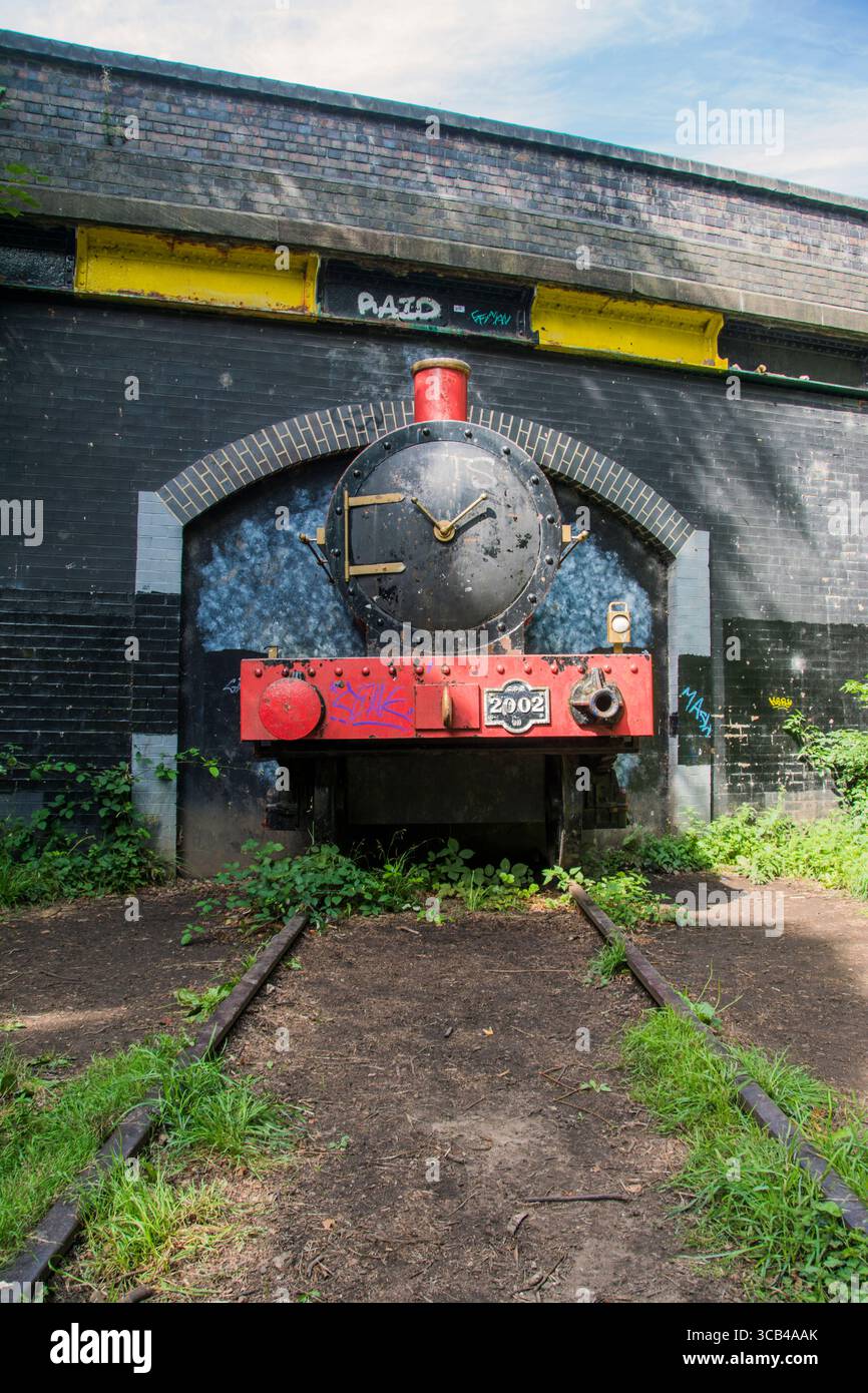 Little Red Train, eine lebensgroße rote Dampflokomotive, die aus einem Tunnel unter einer Brücke hervorgeht Stockfoto