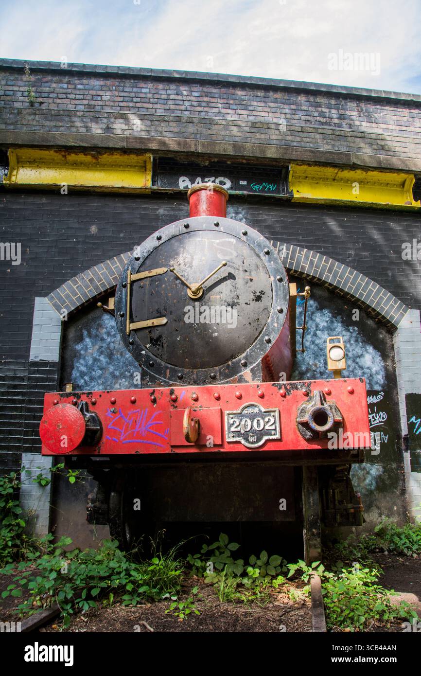 Little Red Train, eine lebensgroße rote Dampflokomotive, die aus einem Tunnel unter einer Brücke hervorgeht Stockfoto