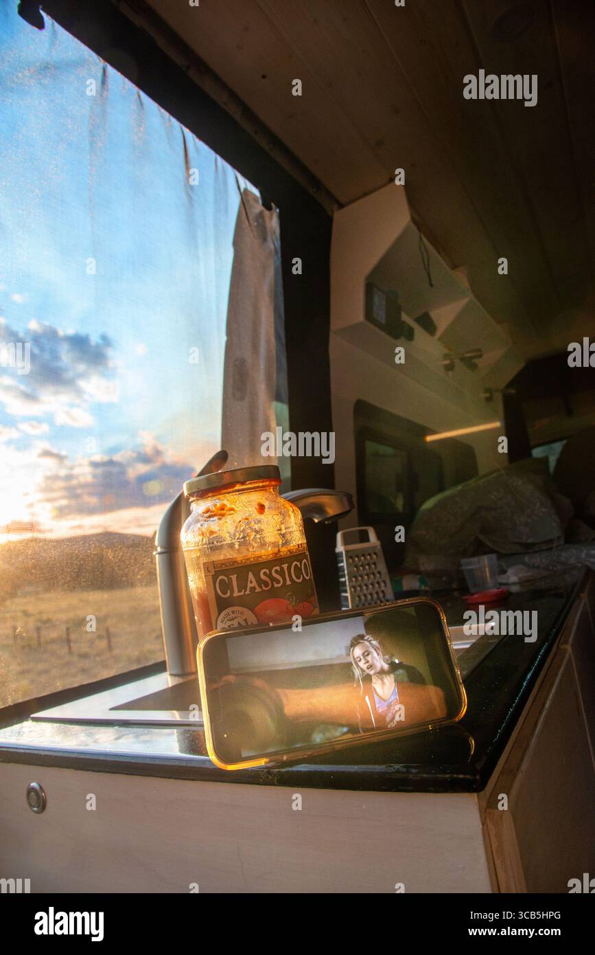 Eine ältere Frau sieht sich einen Film auf ihrem Handy an, während sie im Wald der Elk Mountains im Zentrum von Colorado campt. Stockfoto