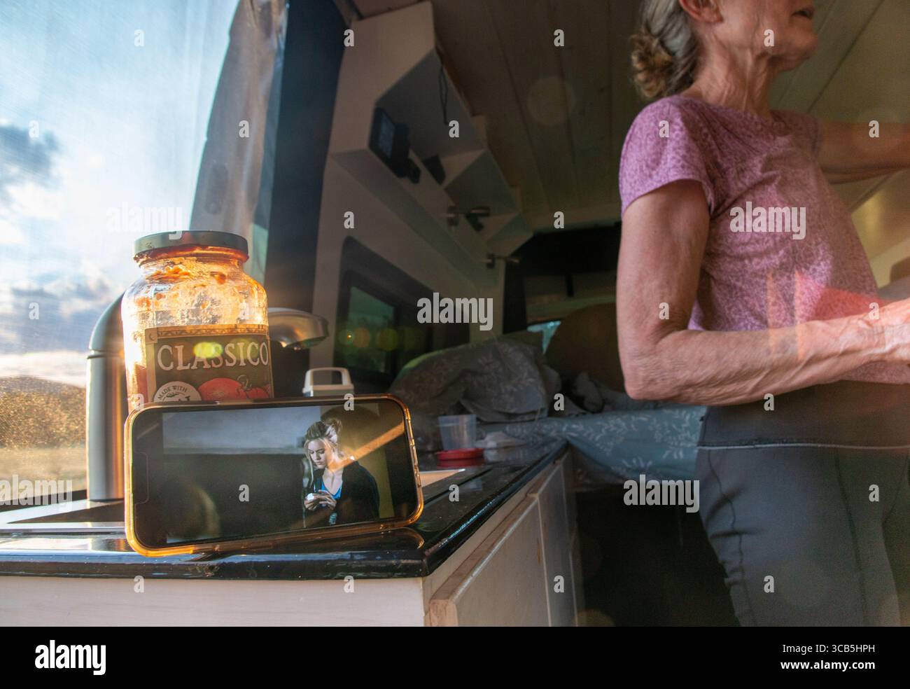 Eine ältere Frau sieht sich einen Film auf ihrem Handy an, während sie im Wald der Elk Mountains im Zentrum von Colorado campt. Stockfoto