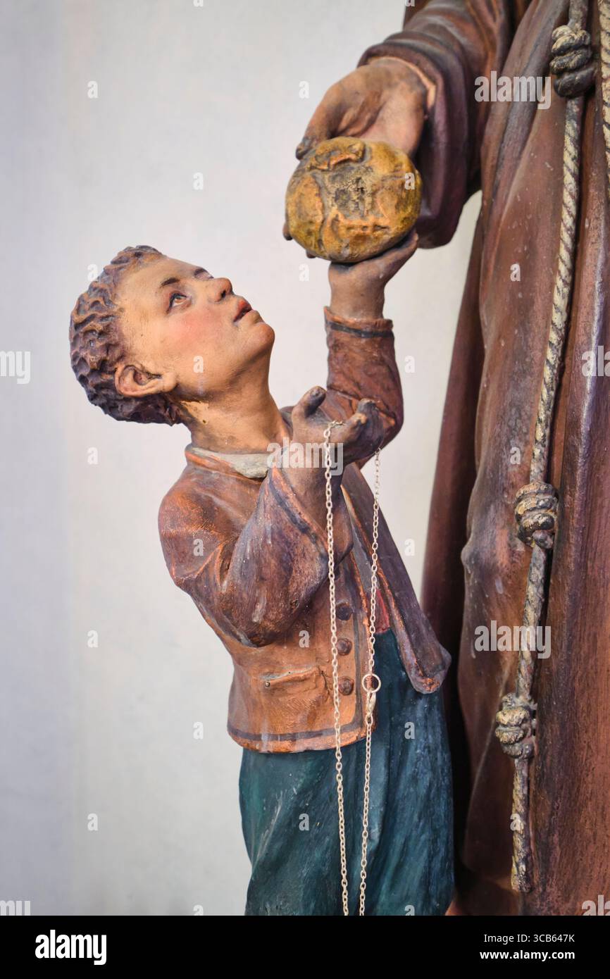 Ein kleiner Junge, der einen runden Brotlaib erhält. Eine kleine Ikone, Reliquie in einer Nische. In der Kirche San Sepolcro in Mailand, Italien. Stockfoto
