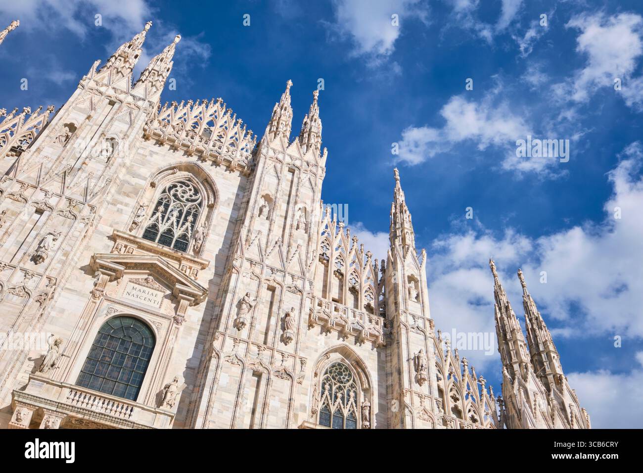 Flacher Blick auf die Vorderfassade an einem sonnigen, klaren Tag mit traumhaft blauem Himmel und weißen, geschwollenen Wolken. Im Duomo in Mailand, Italien. Stockfoto