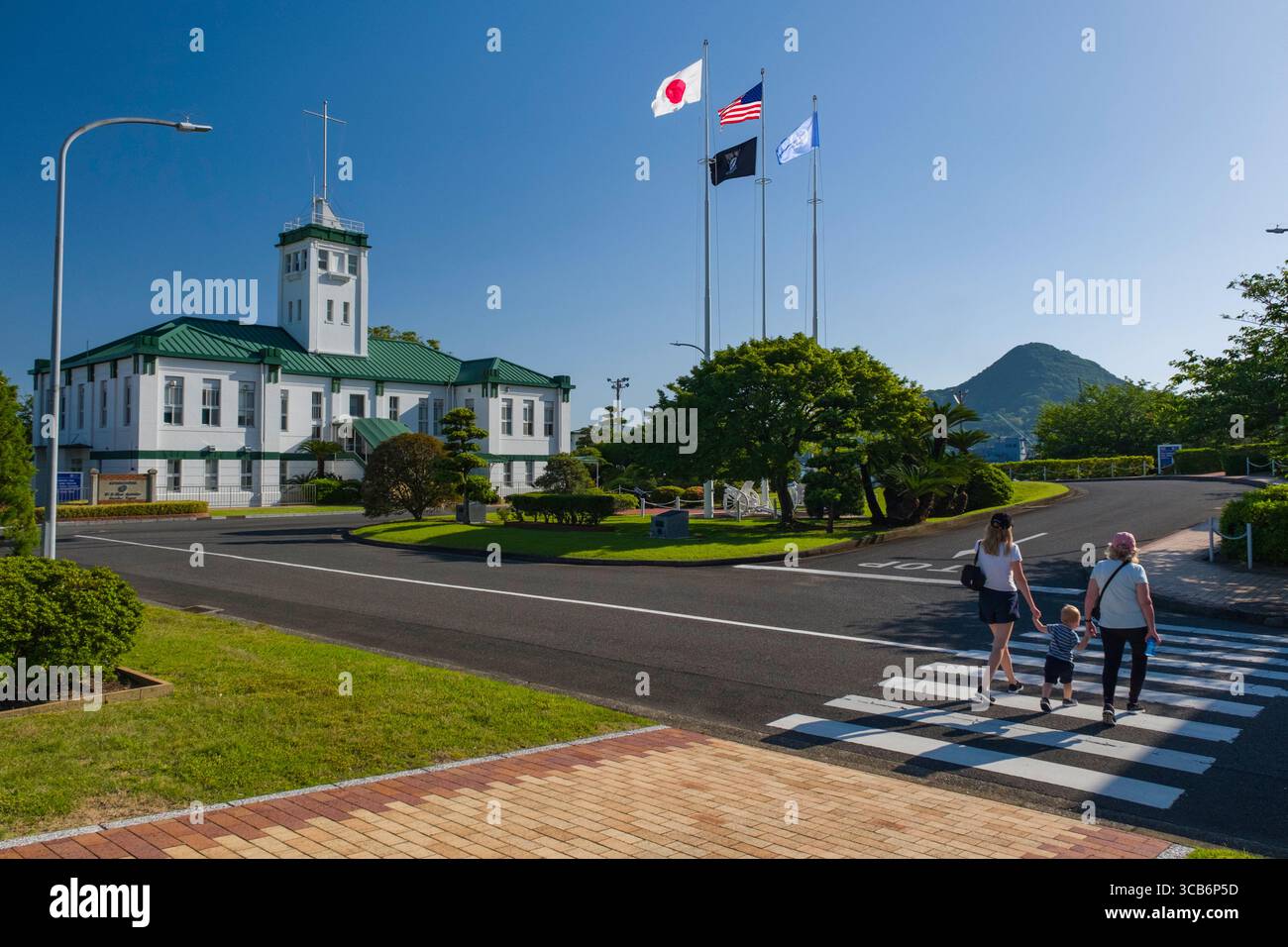 Weißes und grünes Fleet Activities Sasebo Command Hauptquartier mit Nationalflaggen, umgeben von Grün und einem Berg, Sasebo, Japan Stockfoto