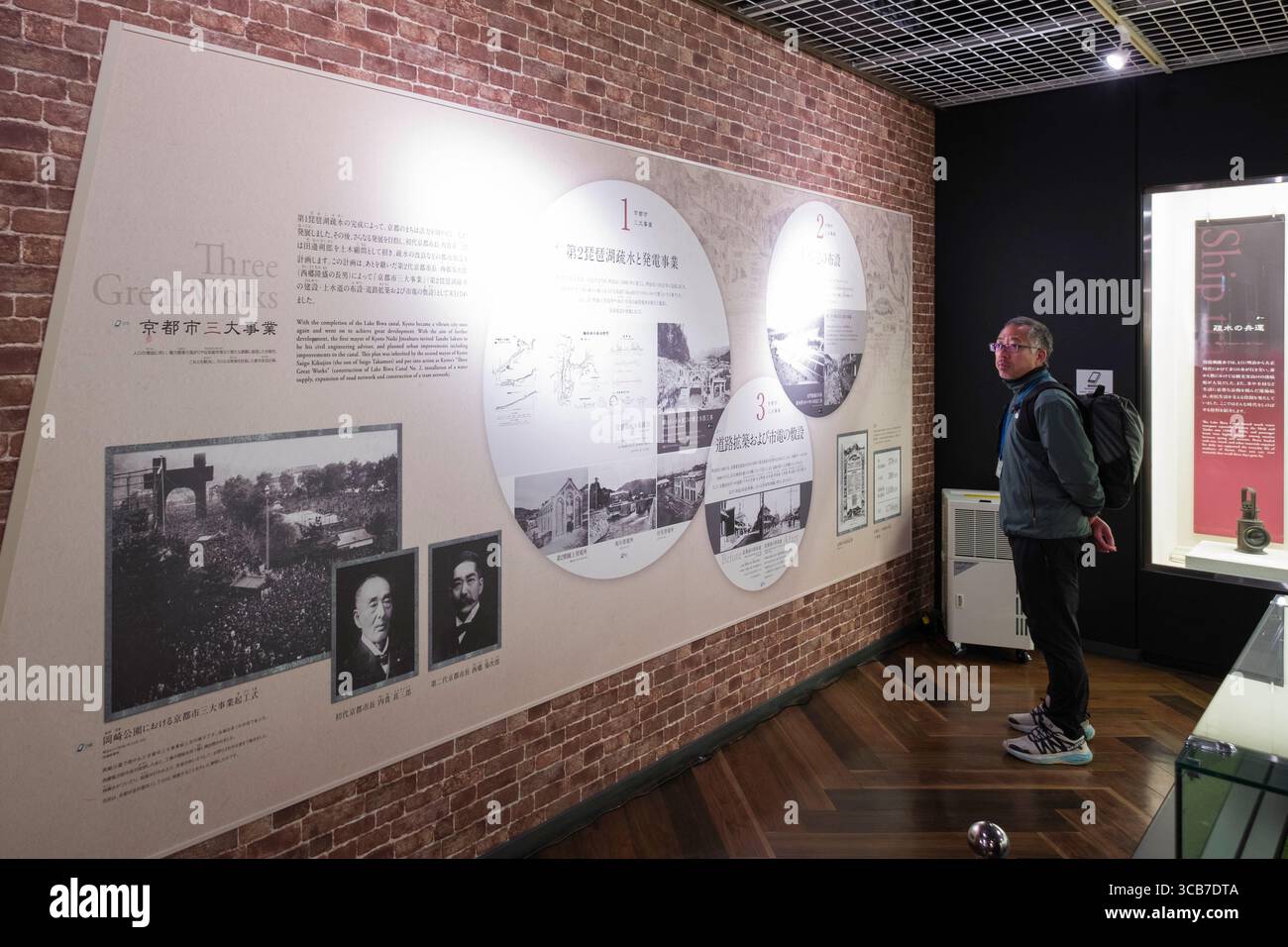 Ein Besucher untersucht aufmerksam die Ausstellung des Lake Biwa Canal Museum mit historischen Inhalten auf einer Mauer mit Backsteinmuster, Kyoto, Japan Stockfoto